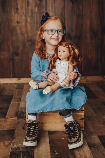 Girl holding her look-alike doll smiling off in the distance