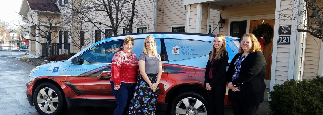 Four women standing in front of a car provided by GM