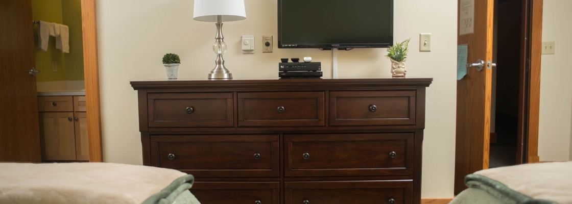 View from in-between two queen beds looking at a dresser, a lamp, and a television